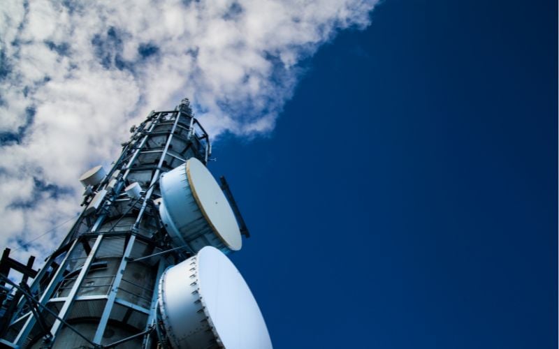 Angled photo of a radio tower playing music in Ireland rising to a bright blue sky with clouds 