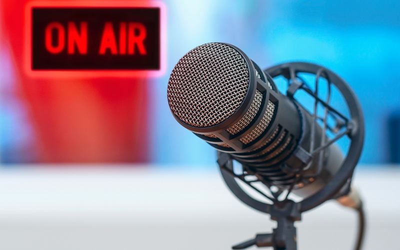 Close-up of a microphone and the words "to broadcast" in the background against a red and blue background