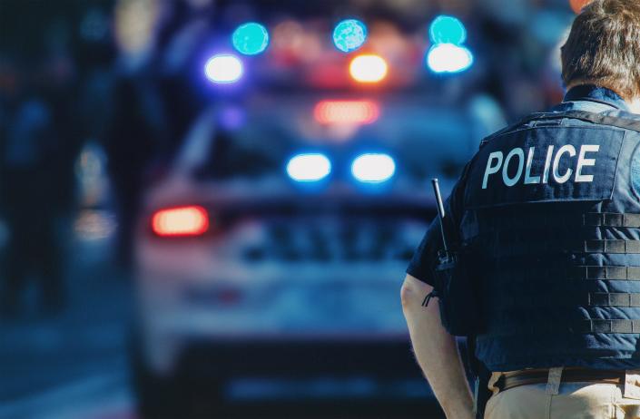 American police officer stands in front of a police car.