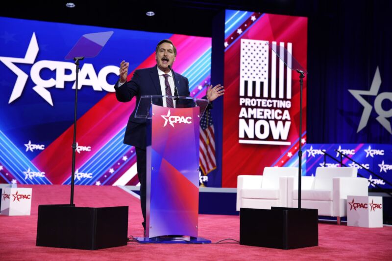 Mike Lindell speaks on stage at the Conservative Political Action Conference, flanked by placards reading 