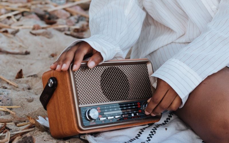 Woman on the beach wearing a white long shirt listening to DAB radio on the sand