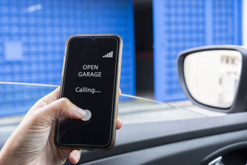 woman in the car using mobile phone to open garage.  woman entering pin in smartphone while unlocking garage.