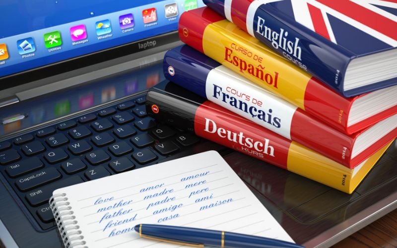 Language books and a notepad with Spanish on an open laptop 