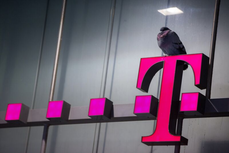 A bird sits atop a T-Mobile sign outside a cell phone store,