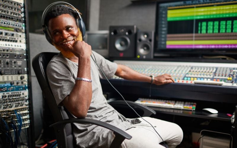 Smiling radio host wearing headphones with his hand on his face, leaning back in his chair at a radio station