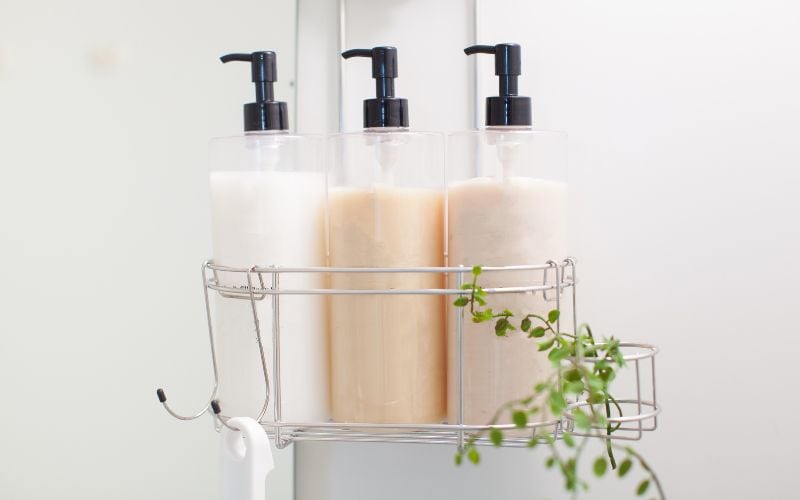 Three shampoo bottles in a caddy with green ivy wrapped around one side