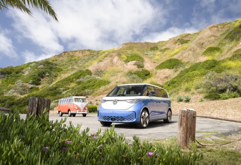 A blue VW ID Buzz and an orange VW T2 with some wild flowers in the foreground