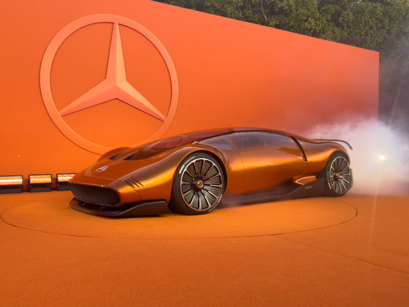 An orange Mercedes concept car next to an orange background.  There's some dry ice fog behind it