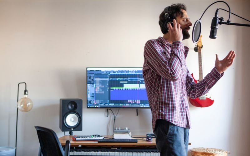 In a simple living room, a man uses a computer, microphone and lamp to record a jingle for a 30-second radio commercial 