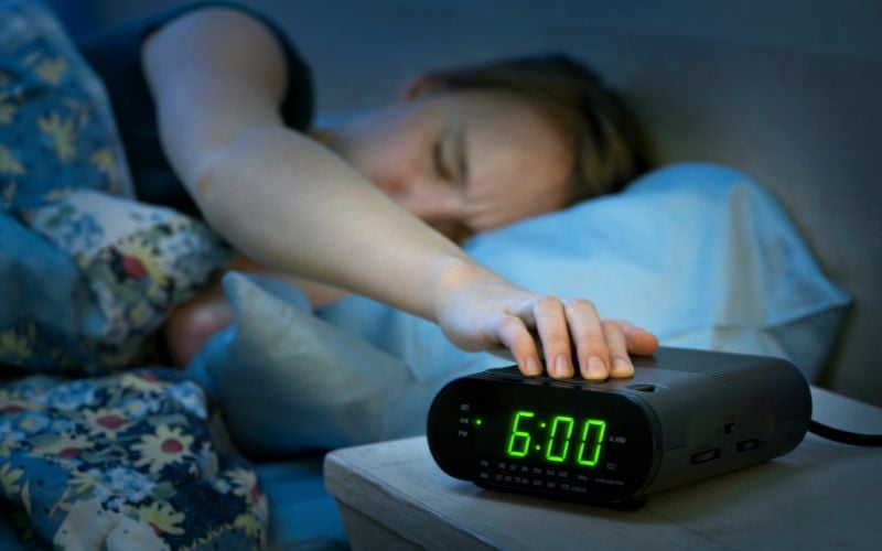 Sleeping woman in bed hits snooze alarm on bedside radio at 6am.  Tecsun radios offer a snooze function