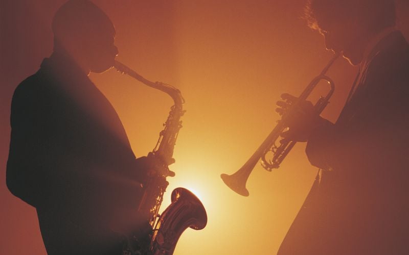 Two jazz musicians perform on stage with orange lights in background 