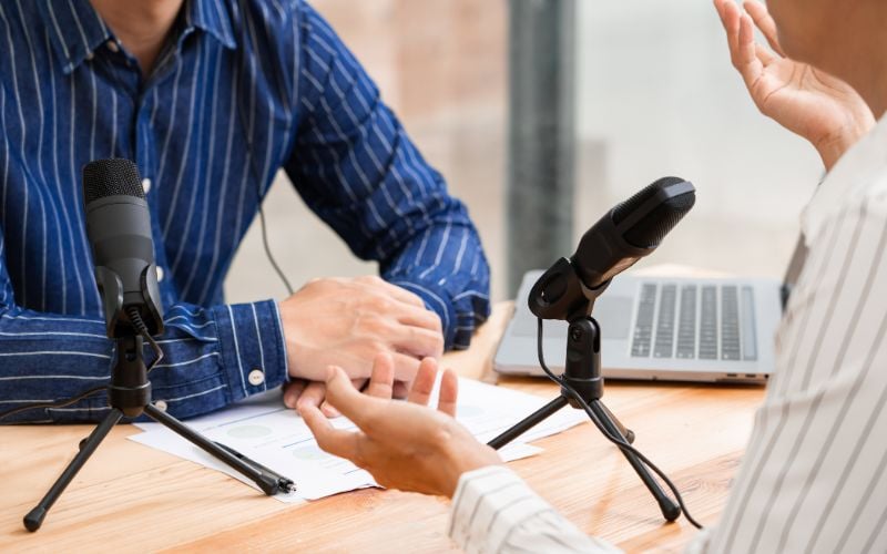 Controversial radio hosts in striped shirts sit across from each other with microphones