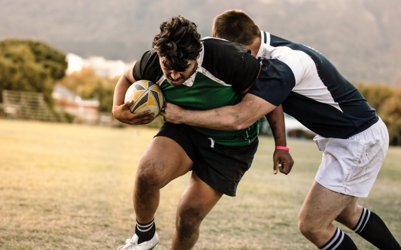 Two men play rugby and compete for position on the pitch