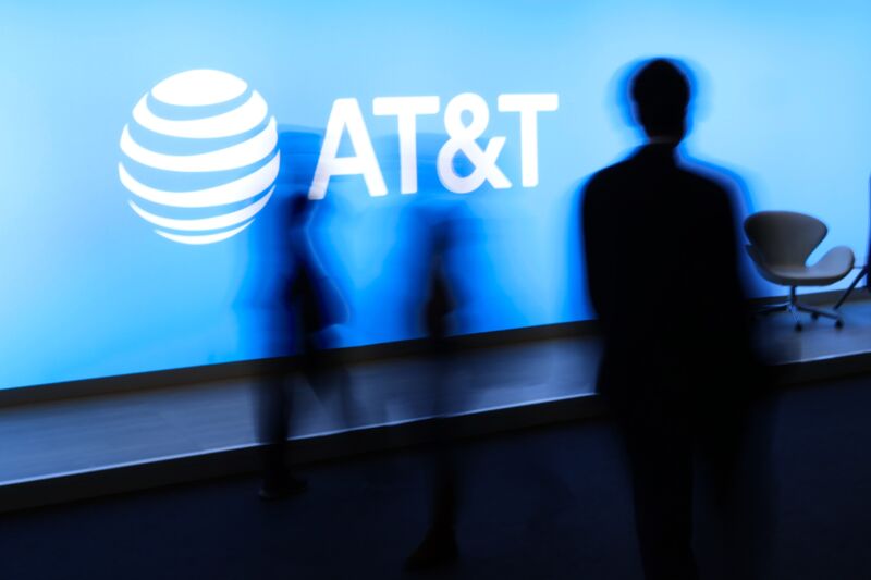 People at a conference walk past a large AT&T logo.