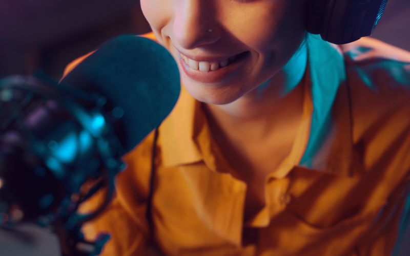 Close-up of a smiling radio host in a yellow button-down shirt in front of a microphone recording a 30-second radio commercial