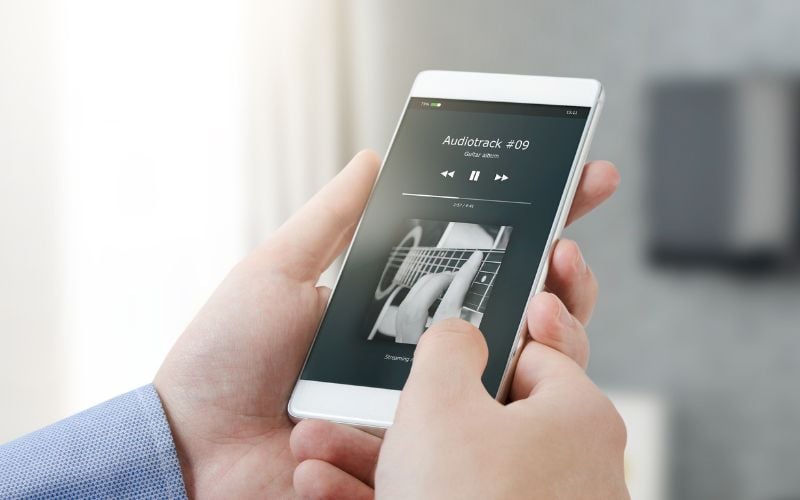 Two hands holding a phone and listening to AM radio on smartphone in a sunny white room