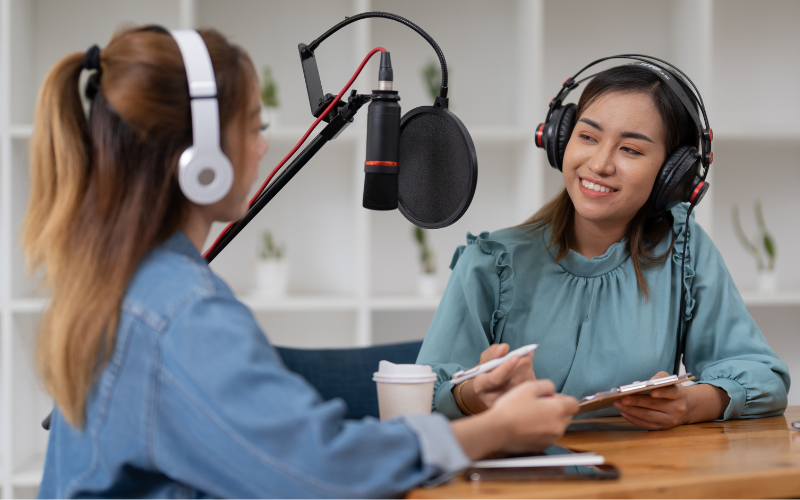 Two women radio presenters are talking, looking at each other and smiling