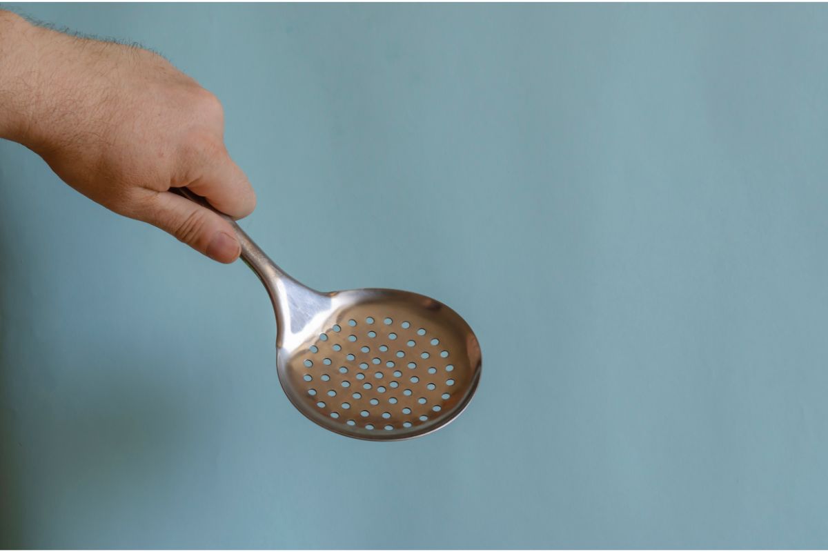 Hand Holds a Metal Slotted Spoon