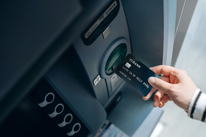 High angle shot of female hand inserting her bank card into an ATM in the city. Withdrawing money, paying bills, checking account balances and making a bank transfer. Privacy protection, internet and mobile banking security concept